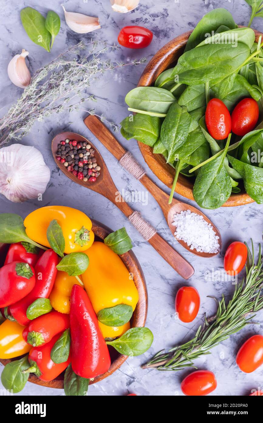 Petits poivrons rouges et jaunes, tomates épinards et cerises, romarin, thym et ail, produits pour faire de la salade végétarienne dans des assiettes en bois Banque D'Images