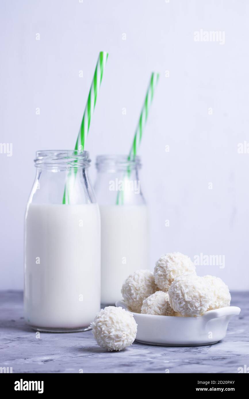 Lait en bouteilles de verre avec pailles vertes et noix de coco blanche bonbons ronds sur table grise sur fond blanc Banque D'Images