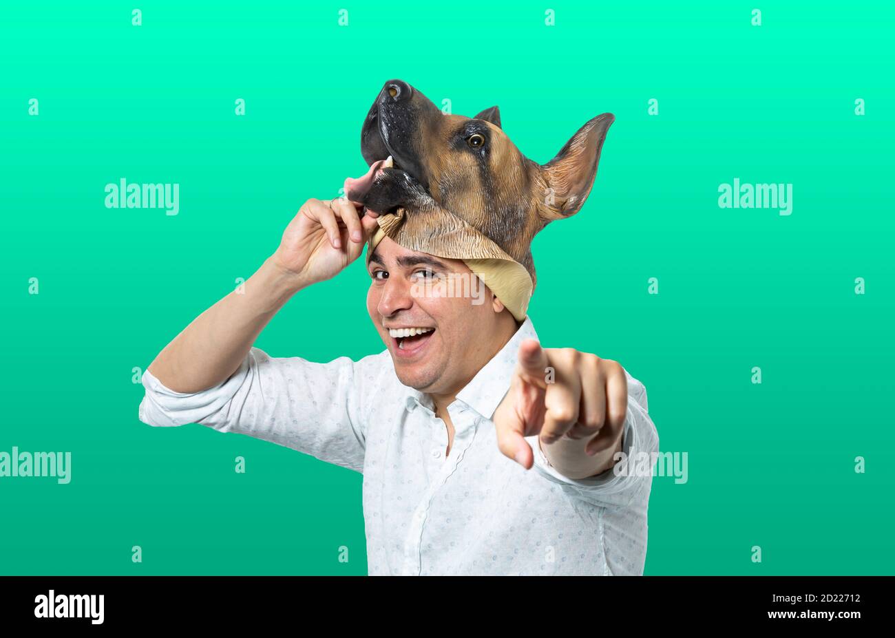 Homme prenant le masque de chien souriant et pointant vers l'appareil photo. Arrière-plan vert isolé. Prise de vue moyenne. Banque D'Images