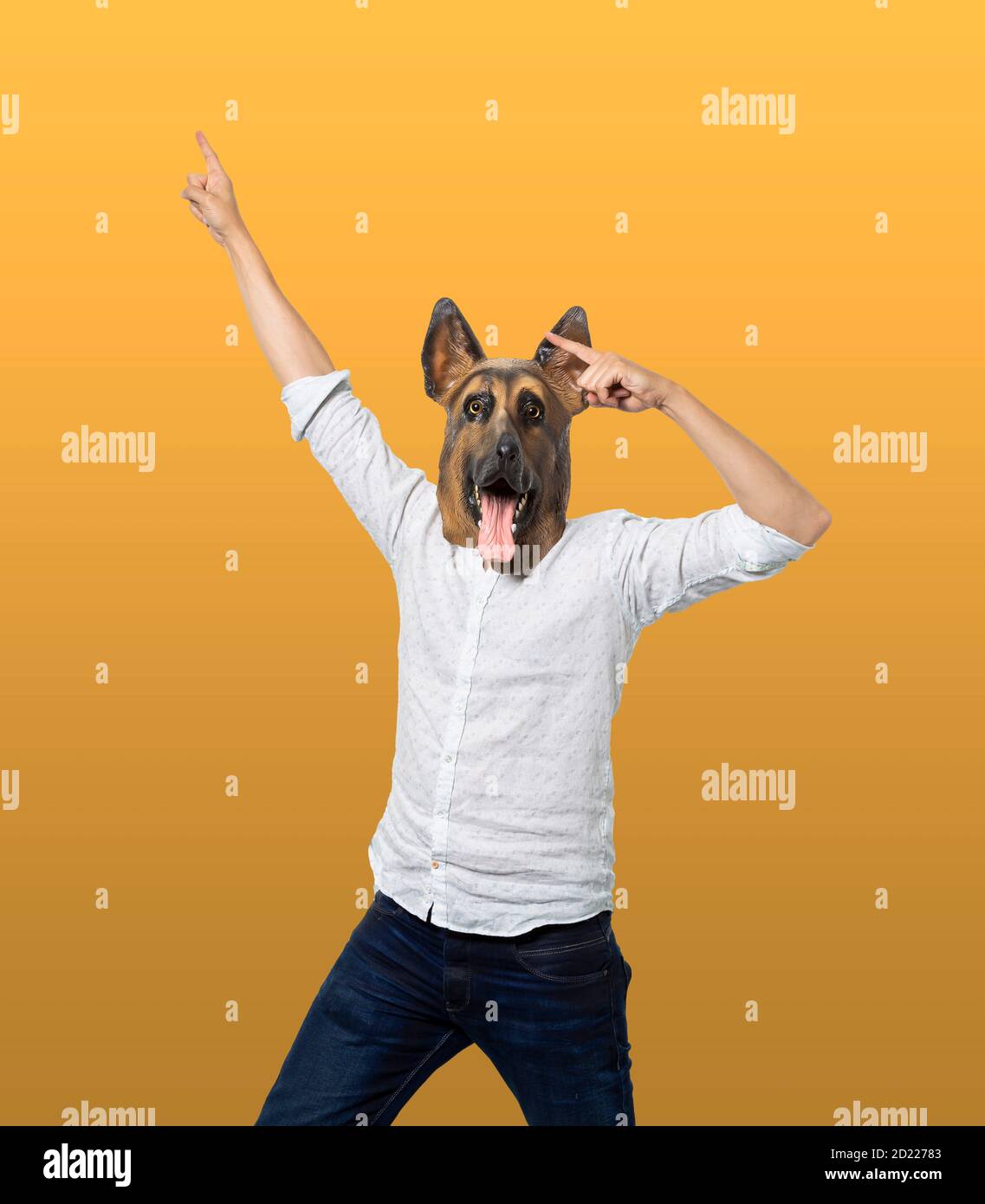 Homme portant un masque de chien regardant l'appareil photo et pointant vers le haut dans la célébration. Arrière-plan jaune isolé. Prise de vue moyenne. Banque D'Images
