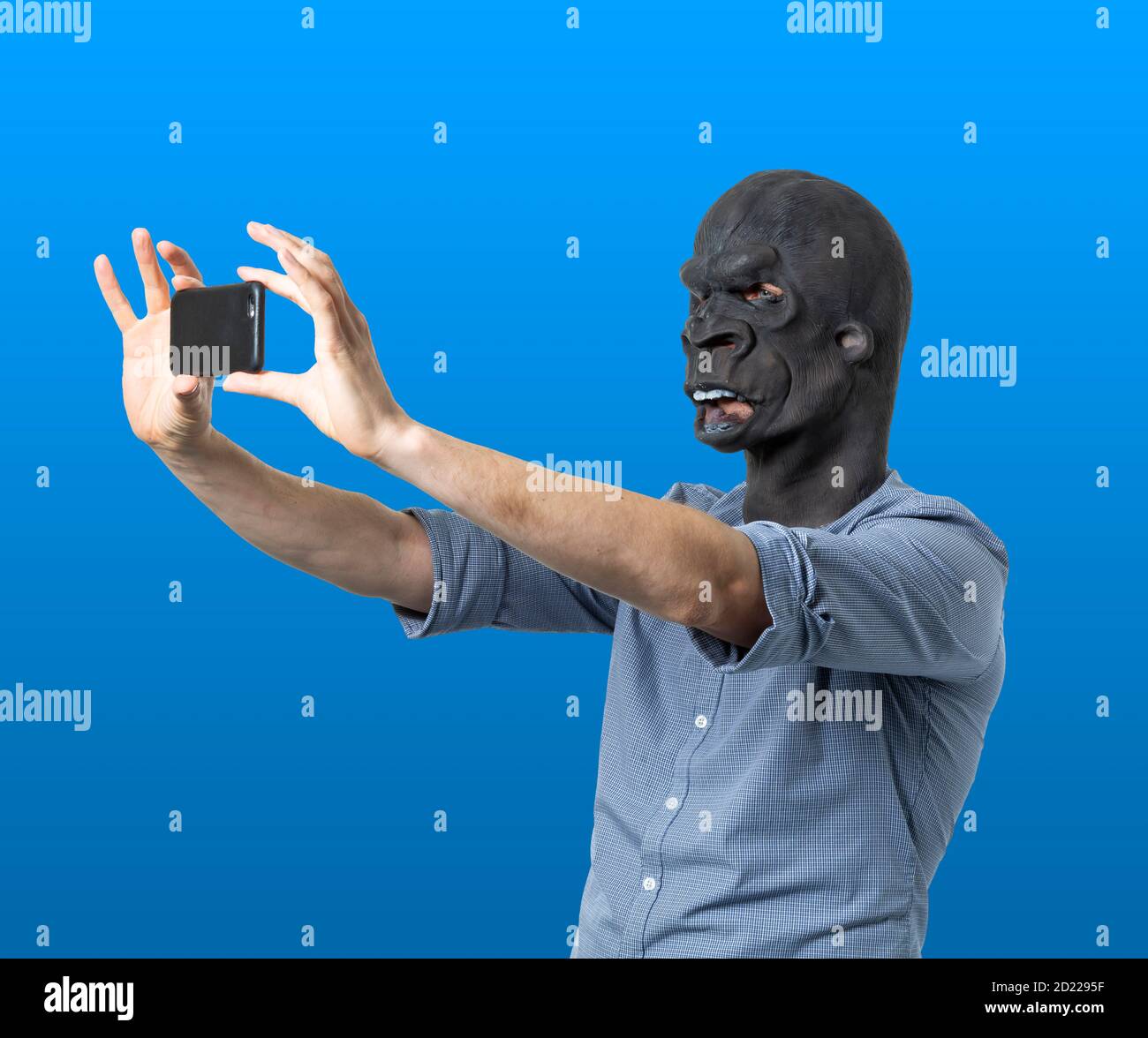 Homme dans le masque de gorille prenant selfie avec le téléphone. Découpe isolée sur fond bleu. Prise de vue moyenne. Vue latérale. Banque D'Images