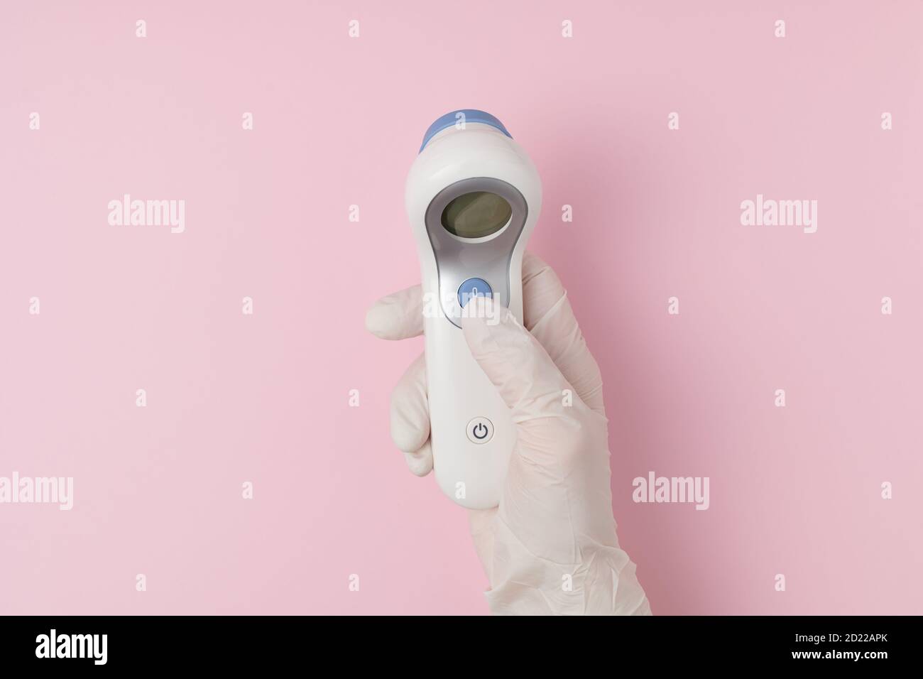 Vue supérieure des mains de femmes avec des gants en caoutchouc blanc et un thermomètre numérique sur fond rose. Banque D'Images