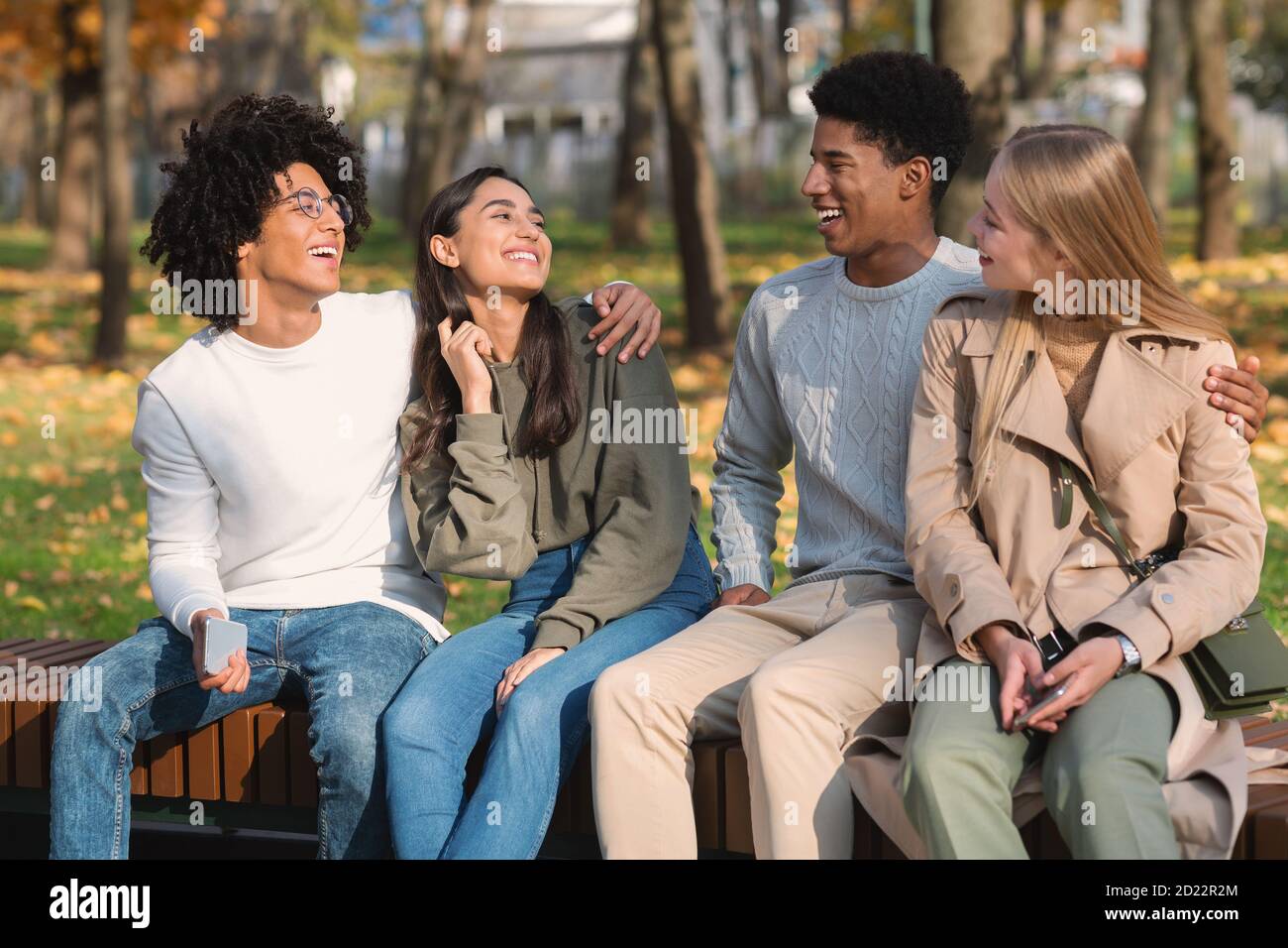 Couples d'adolescents de course mixte assis sur le banc dans le parc public Banque D'Images