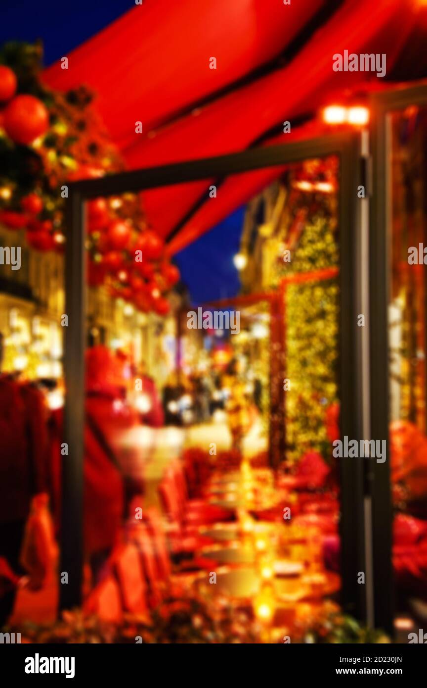 Photo floue de la terrasse du café parisien décorée pour Noël. Feux de rue en soirée. Les gens avec des sacs d'achats dans la rue - acheter des cadeaux. Banque D'Images