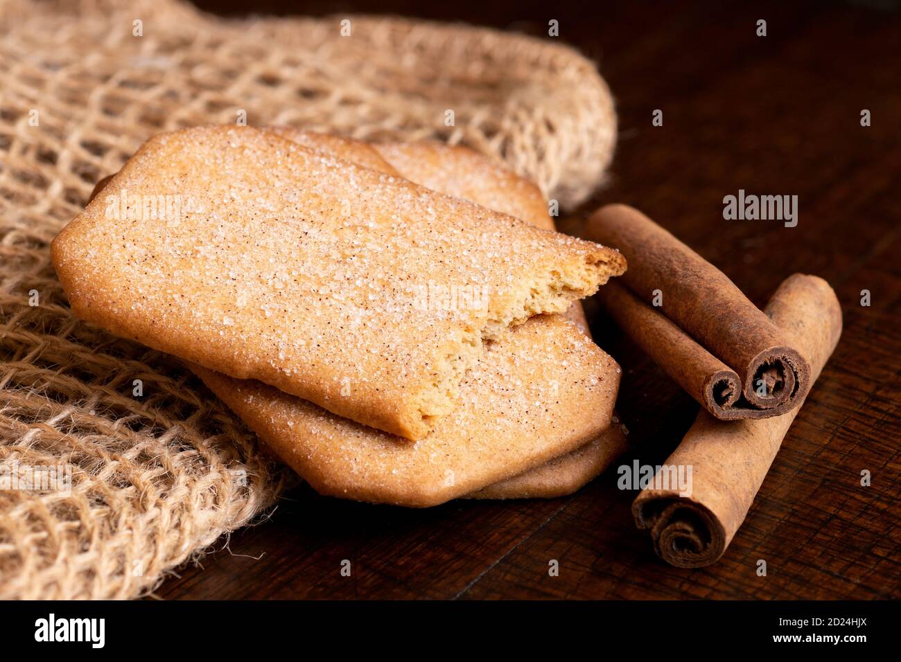 Deux et demi-biscuits rectangulaires à la cannelle enrobés de sucre à côté de bâtons de cannelle sur table en hessian et en bois sombre. Banque D'Images