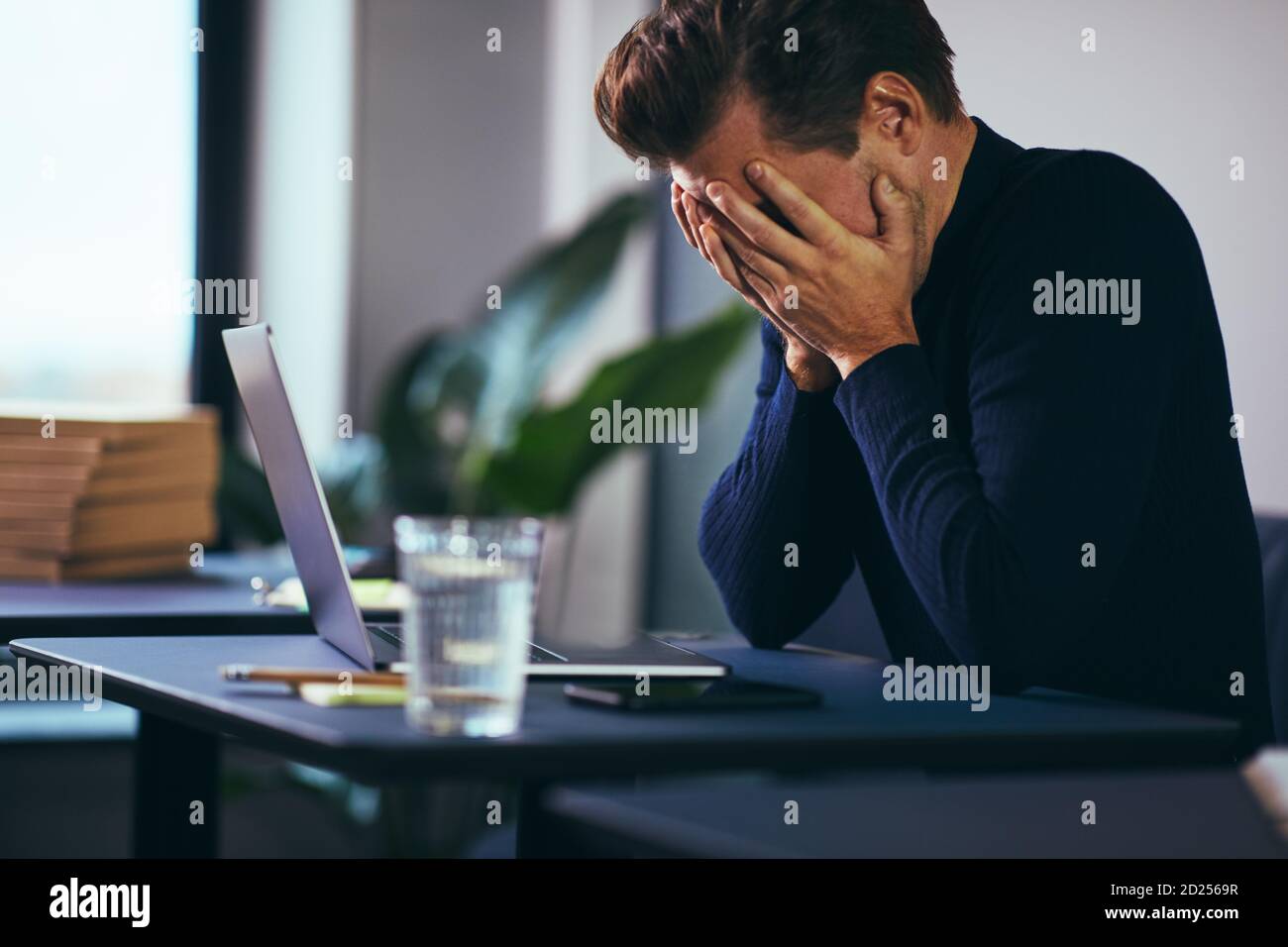 Jeune homme d'affaires assis avec sa tête dans les mains frustration en travaillant sur un ordinateur portable à un bureau Banque D'Images
