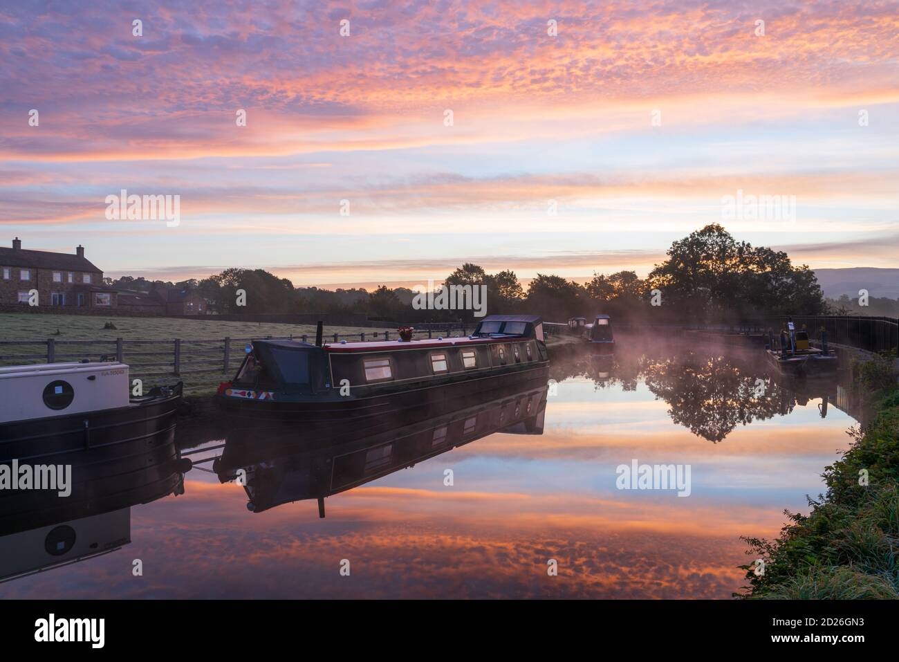 Un superbe lever de soleil au-dessus du canal de Leeds et Liverpool à Skipton, dans le parc national de Yorkshire Dales, tandis que les bateaux-canaux flottent sur le miroir de l'eau calme. Banque D'Images