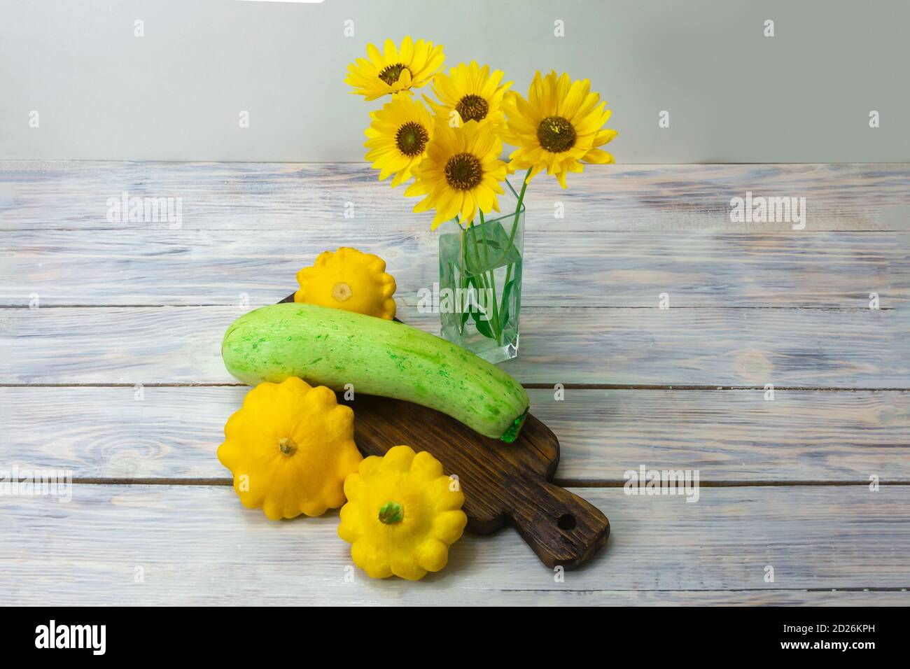 La courge verte et la mini patty jaune écrasez sur une table en bois. Belles fleurs jaunes dans un vase en verre. Banque D'Images