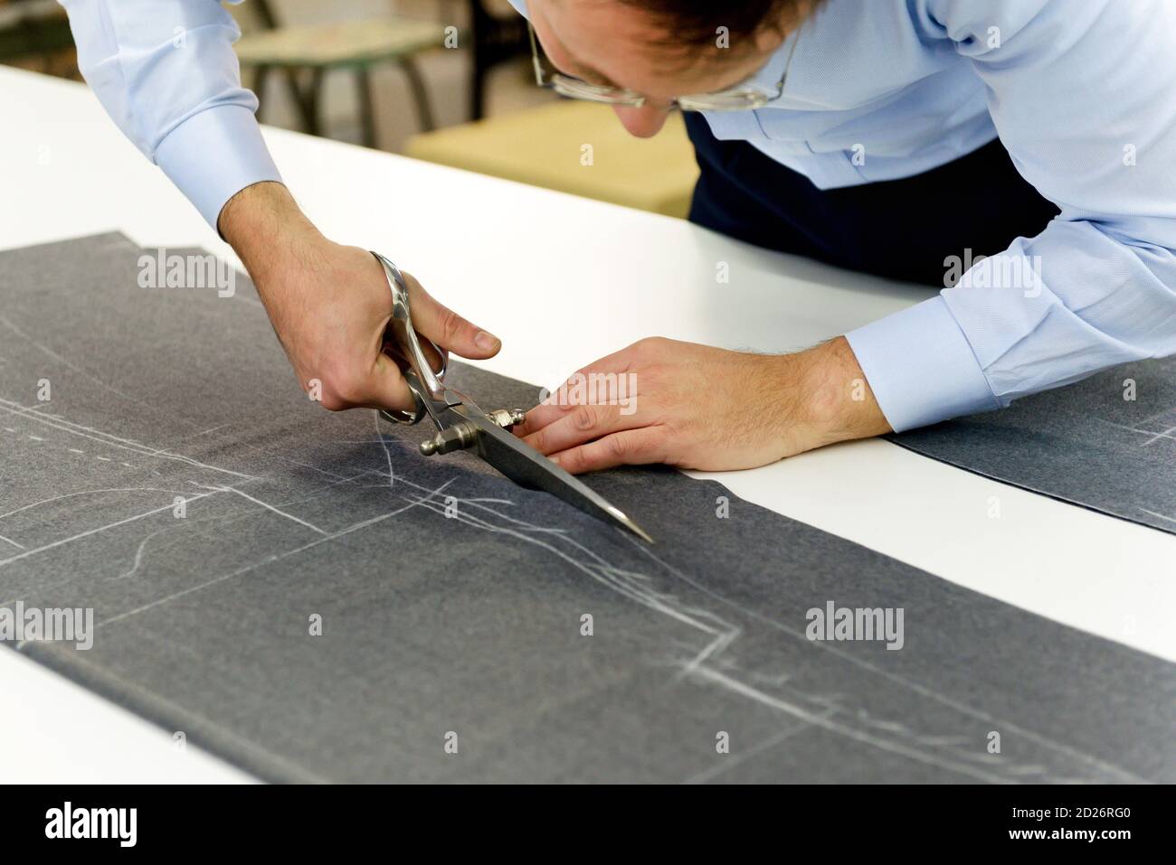 Tailler soigneusement le tissu gris dans un atelier en utilisant de grands cisaille pour suivre le motif craqué sur le textile comme il fabrique des vêtements sur mesure Banque D'Images