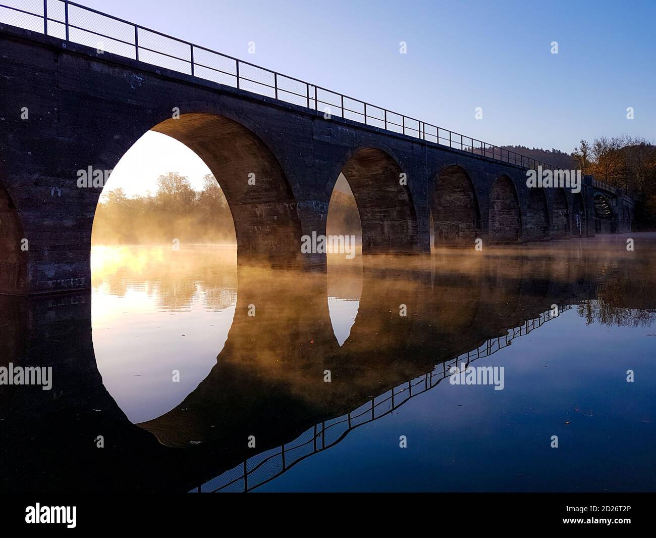 Soleil brillant à travers un pont sur un lac calme Banque D'Images