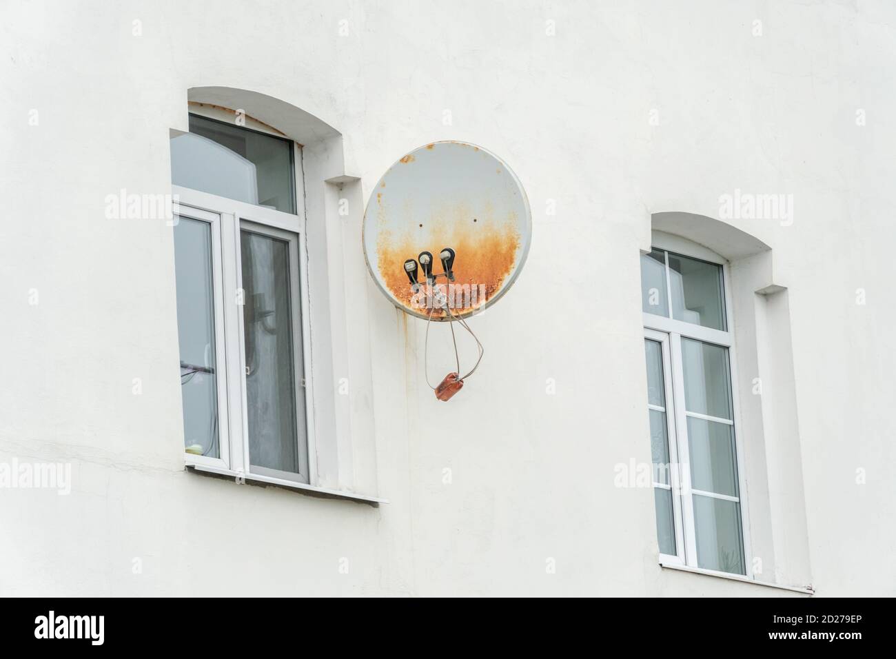 Plat satellite rouillé sur le mur blanc de la maison avec les vitres en gros plan Banque D'Images