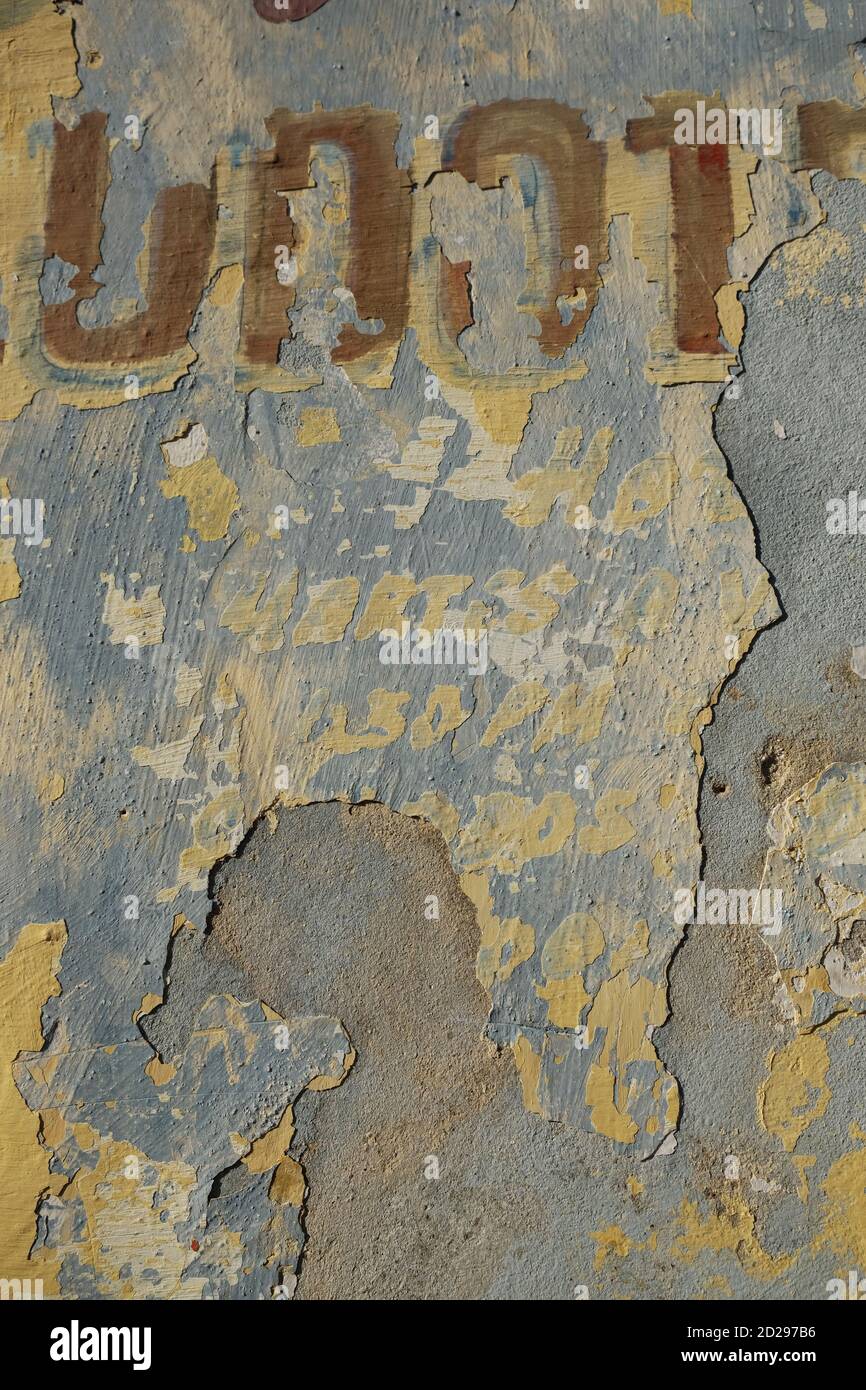 Mur peint et abîmé avec des lettres blanches, rouges, bleues où la peinture s'écaille et rouges Banque D'Images