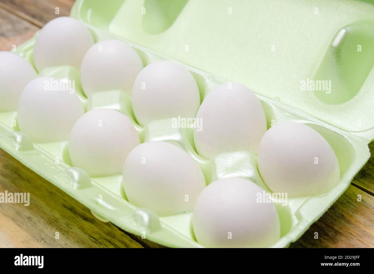 Œufs blancs dans un emballage en plastique vert sur fond de bois gros plan Banque D'Images