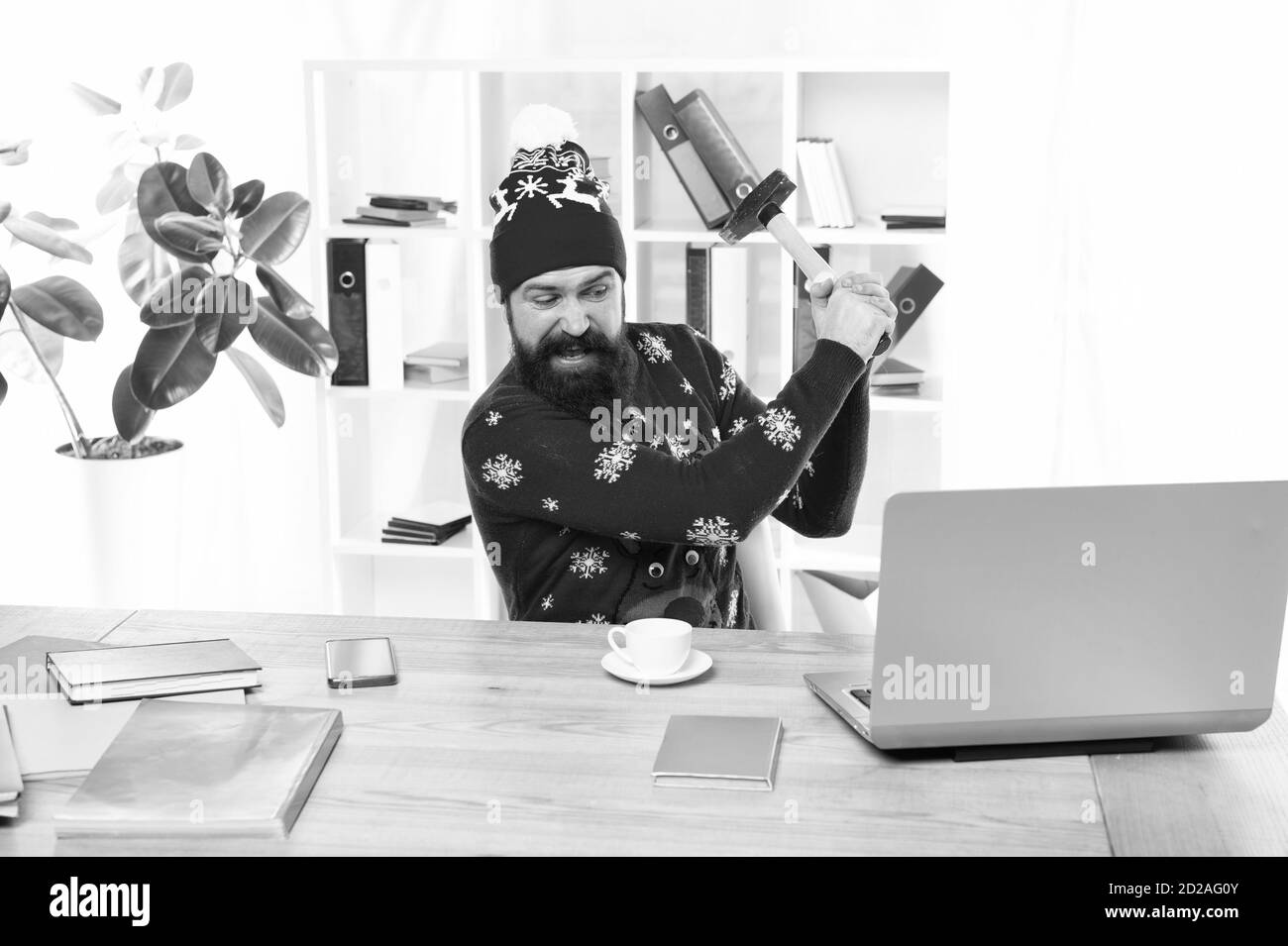 De mauvaises nouvelles. Hipster en colère a frappé un ordinateur portable avec un marteau. Homme barbu dans l'usure de Noël s'est mis en colère. Être en colère à propos de problèmes d'entreprise. Le stress en milieu de travail. Se sentir en colère. Mauvaise humeur. Banque D'Images