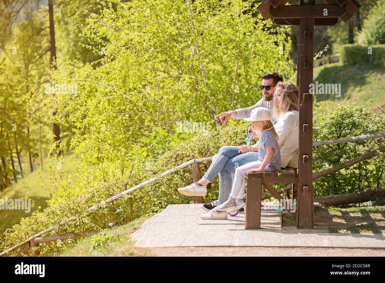 Le père, la mère et leur petite fille sont assis sur le banc en bois un jour de printemps ensoleillé. Banque D'Images