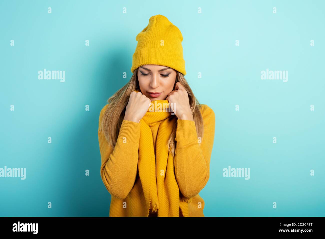 La femme garde au chaud avec un foulard et un chapeau en hiver. Fond cyan Banque D'Images