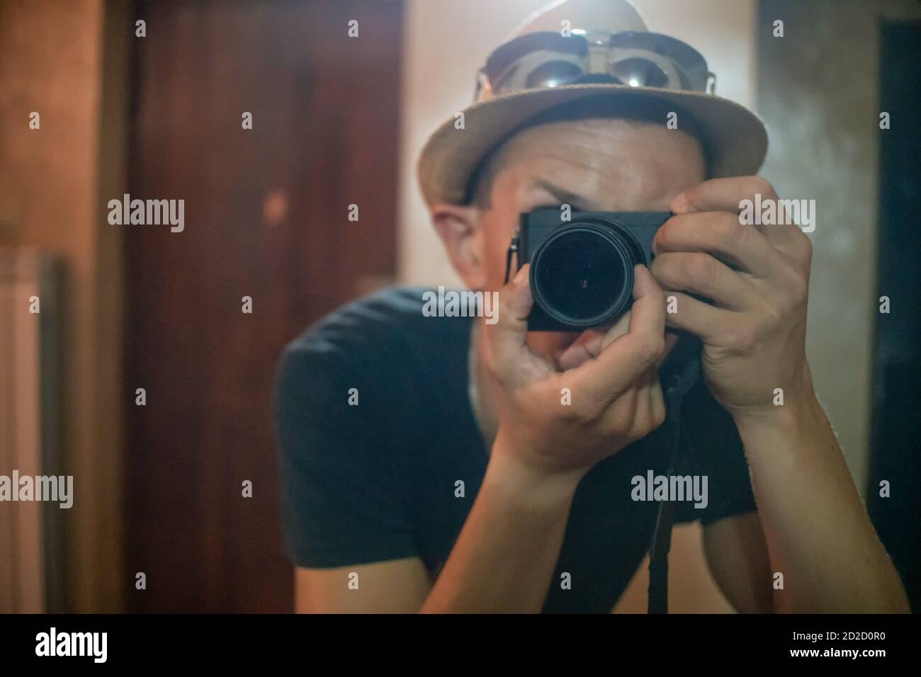 Un jeune homme dans un chapeau de paille et des lunettes fait selfie photo à travers un miroir avec la mise au point sur l'objectif de l'appareil photo. Banque D'Images