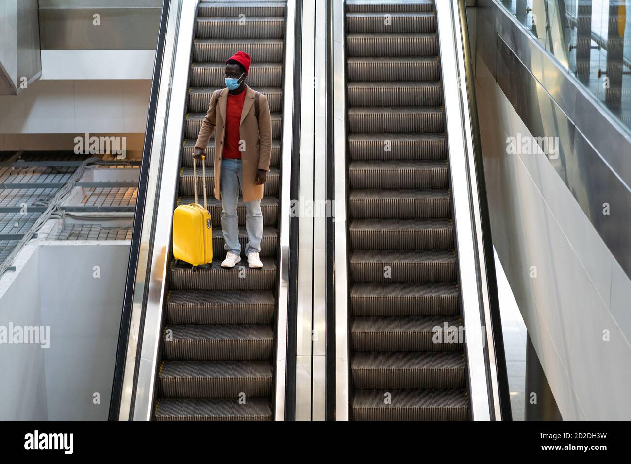 Vue de dessus de l'homme noir avec des bagages jaunes debout sur l'escalier roulant au terminal de l'aéroport portant un masque de protection du visage pendant l'épidémie de virus, Covid-19 pande Banque D'Images