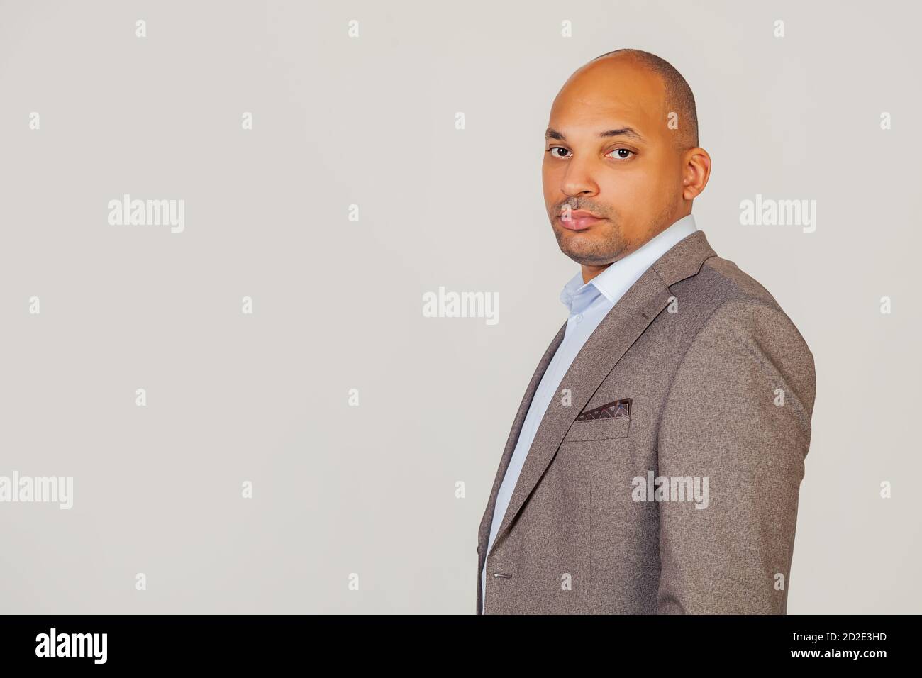 Beau jeune homme d'affaires afro-américain en veste regardant la caméra tenant sa tête dans les trois quarts avec une expression sérieuse sur son visage. Posant pour une photo sur fond gris. Banque D'Images