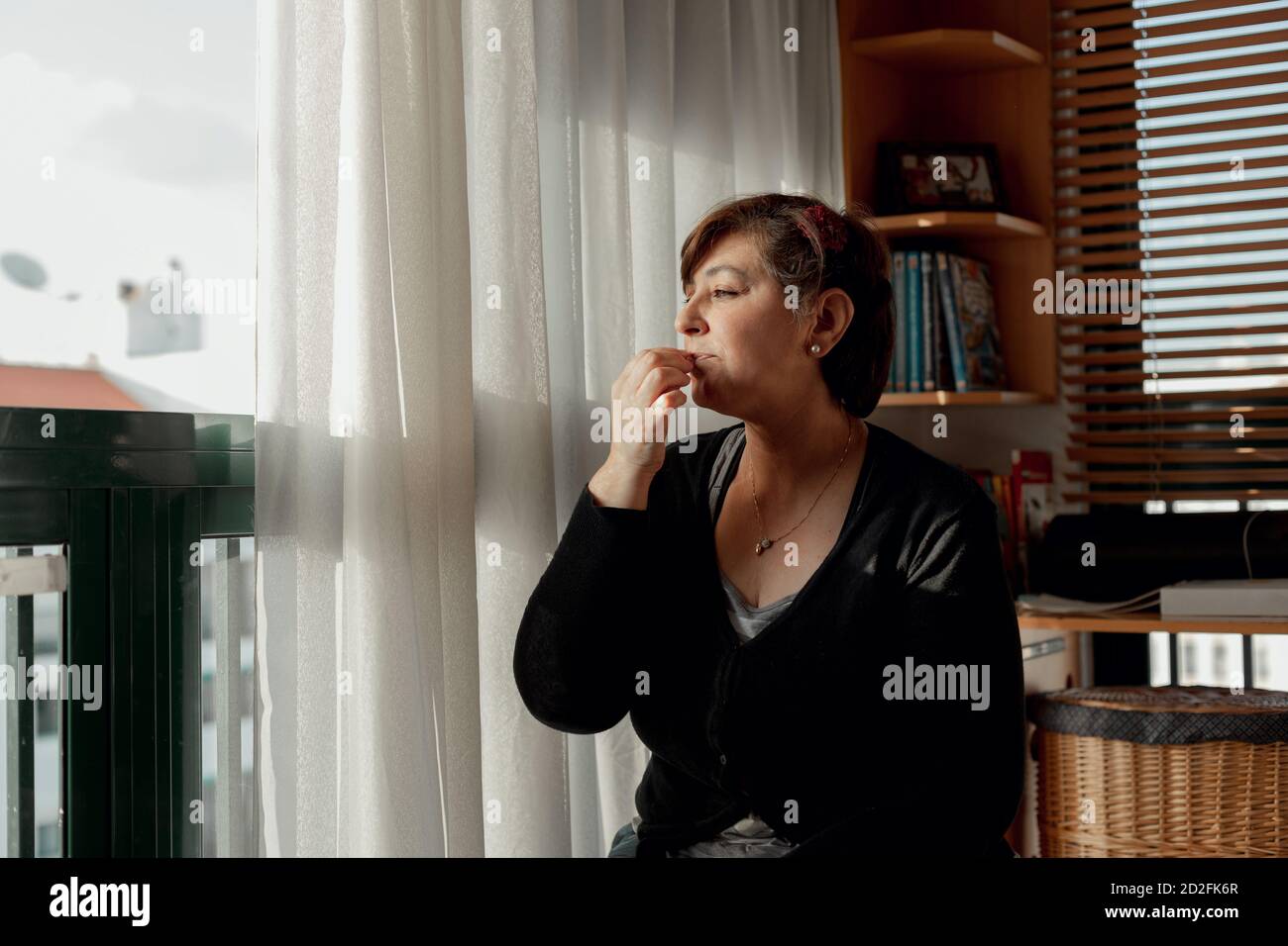 Femme adulte avec des cheveux courts passer du temps assis et se détendre dans son studio tout en mangeant quelques arachides. Passer du temps à se détendre en quarantaine. Banque D'Images