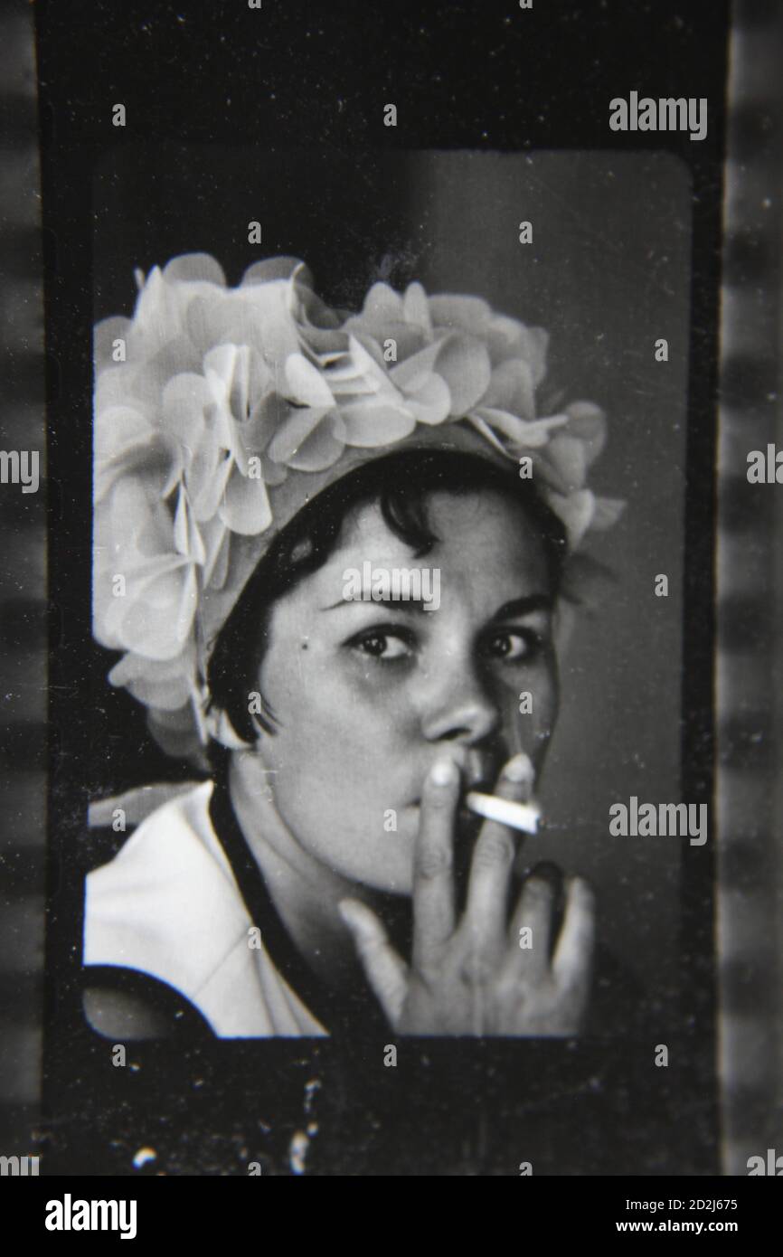 Fin années 1970 photographie vintage en noir et blanc d'une femme portant un chapeau amusant et fumant une cigarette. Banque D'Images