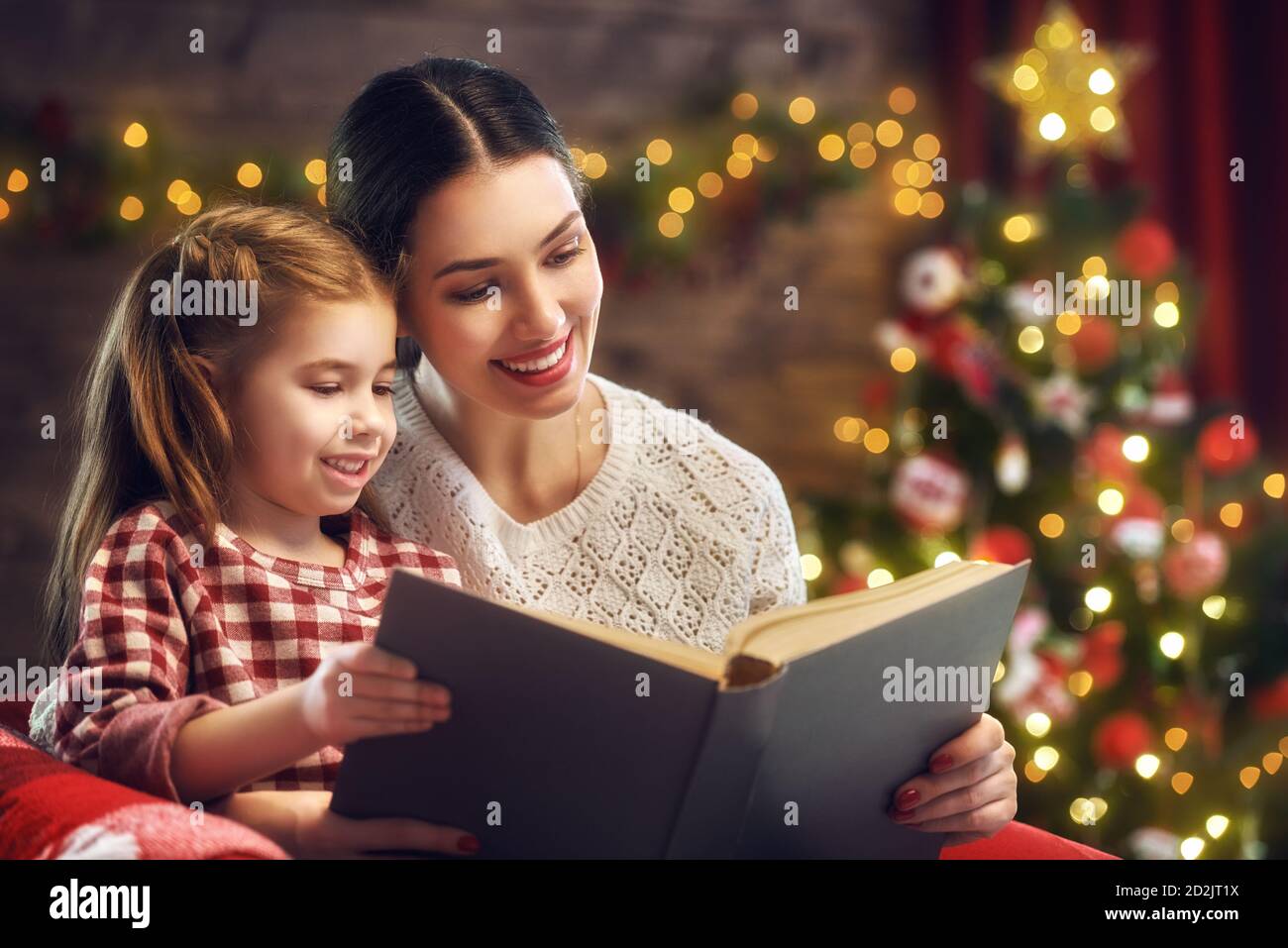 Joyeux Noël et de bonnes vacances ! Jolie jeune maman lire un livre à son joli fille près de l'arbre de Noël à l'intérieur. Banque D'Images