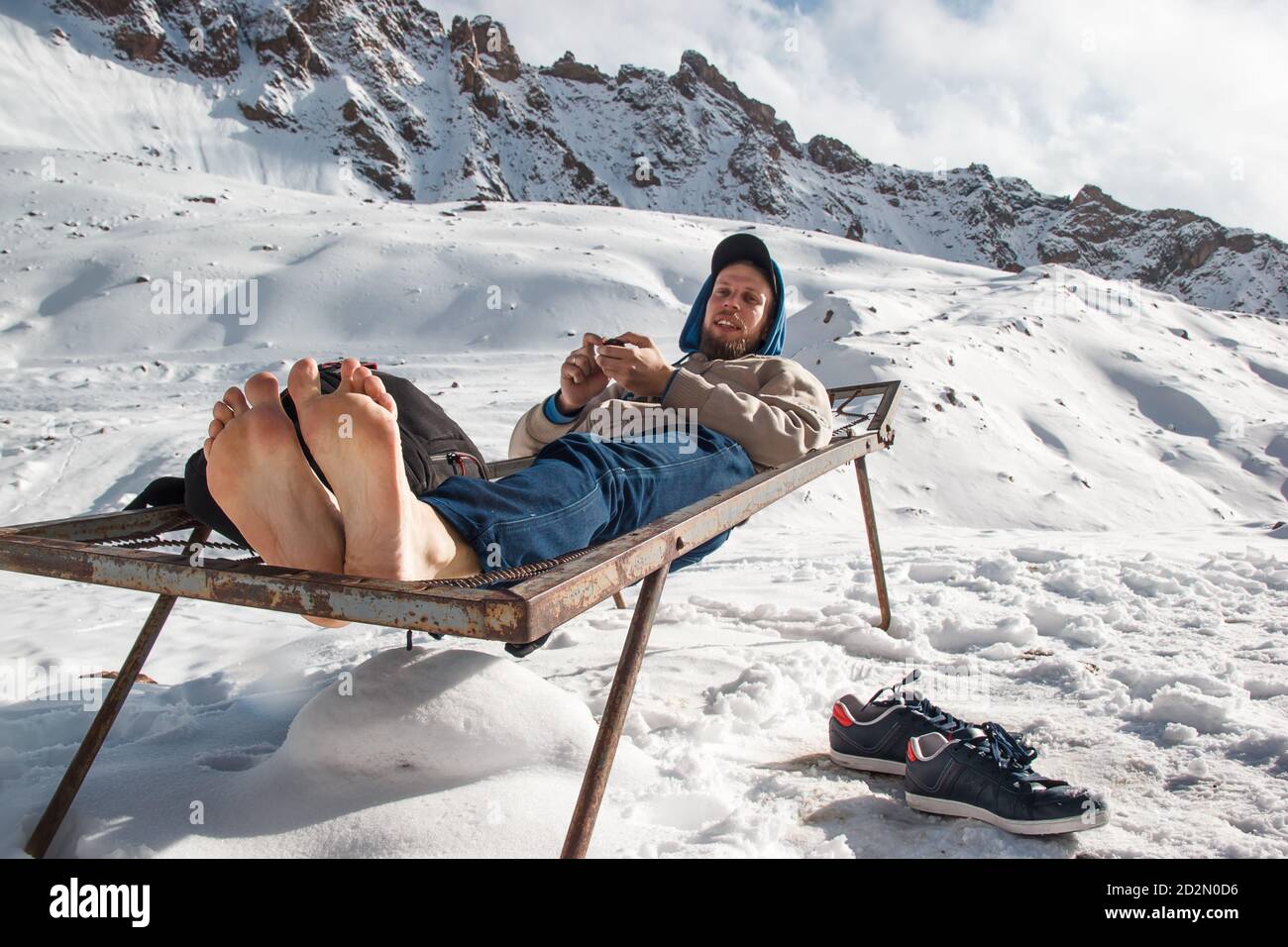 En hiver, un homme aux pieds nus repose sur un lit de fer dans les montagnes. Concept amusant de vacances d'hiver Banque D'Images