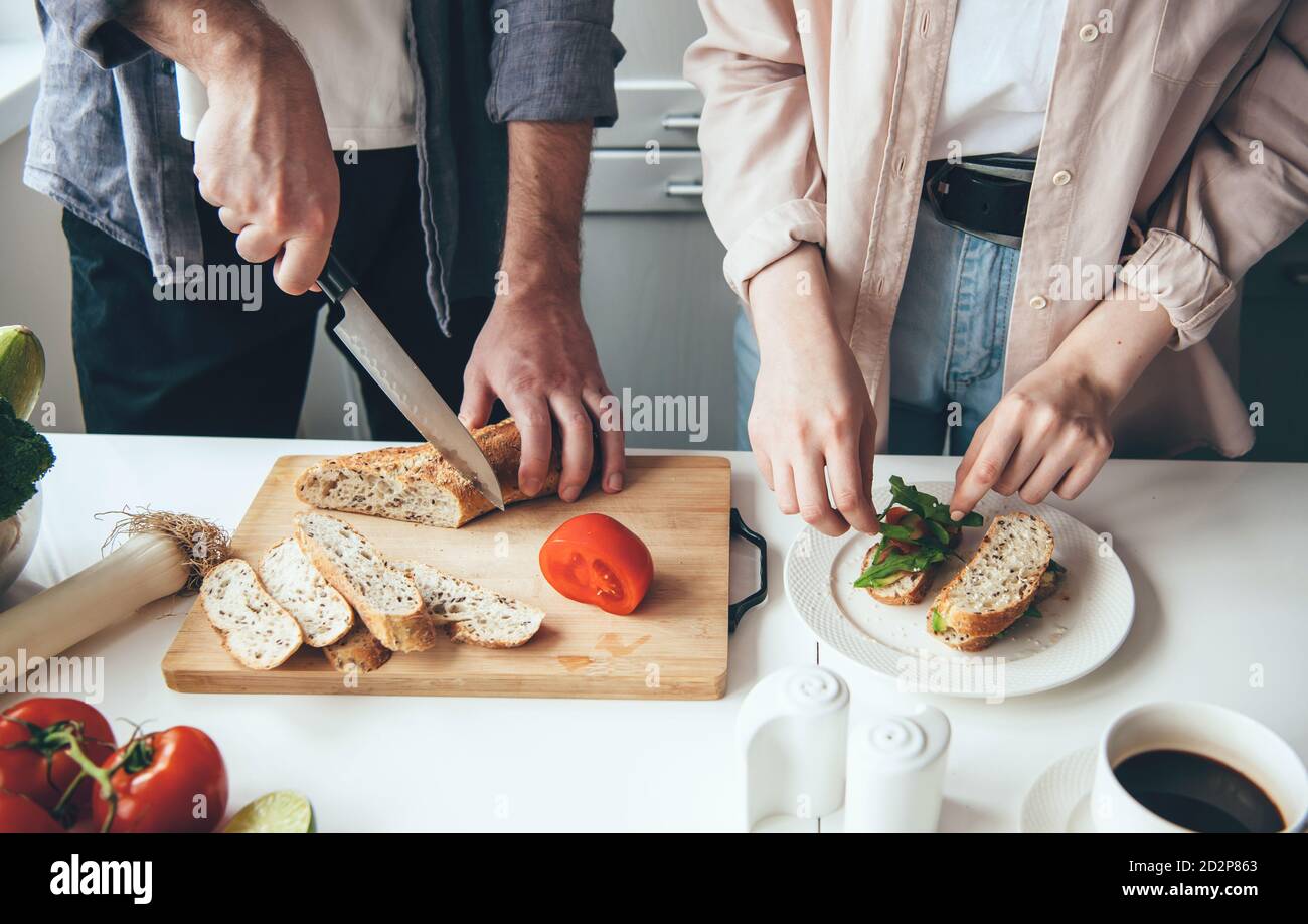 Couple caucasien préparant des sandwichs ensemble tout en tranchant du pain et des légumes dans la cuisine Banque D'Images