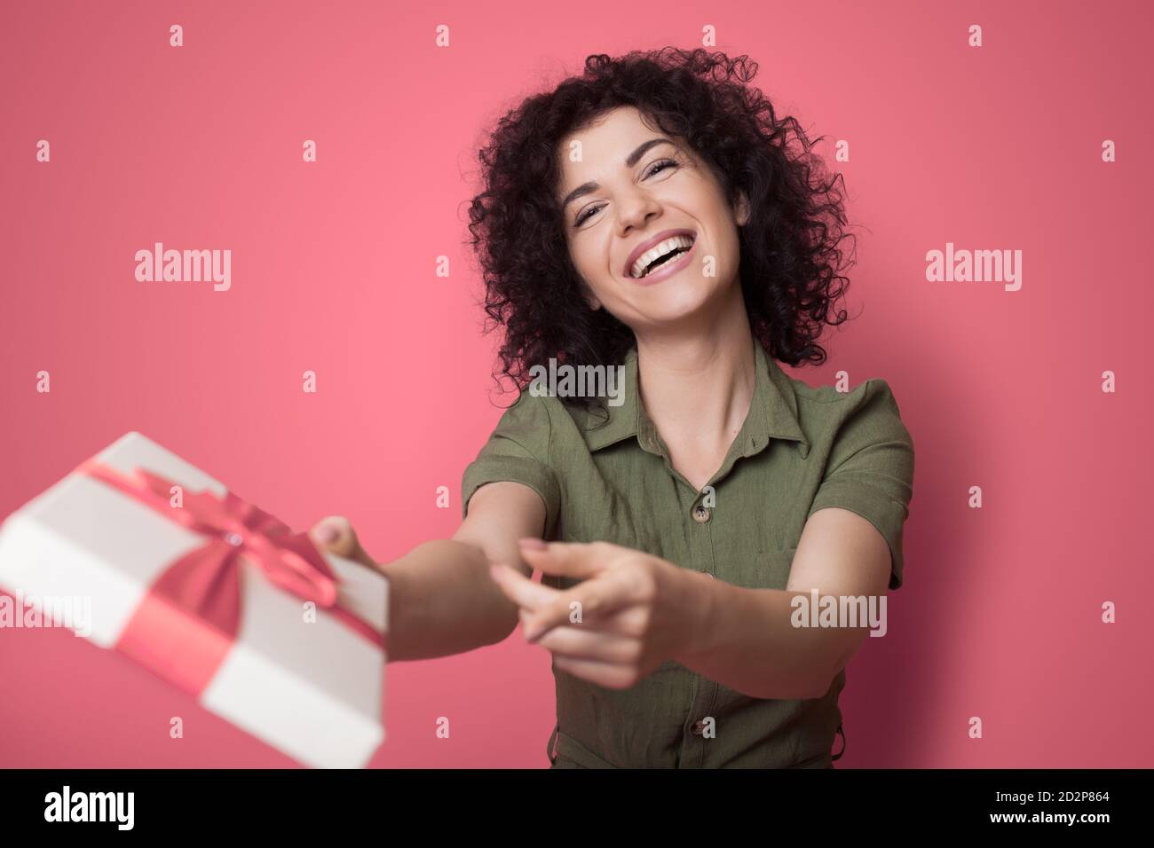 Une charmante dame brune est souriante tout en recevant une boîte cadeau bien emballé sur un mur rouge au studio Banque D'Images