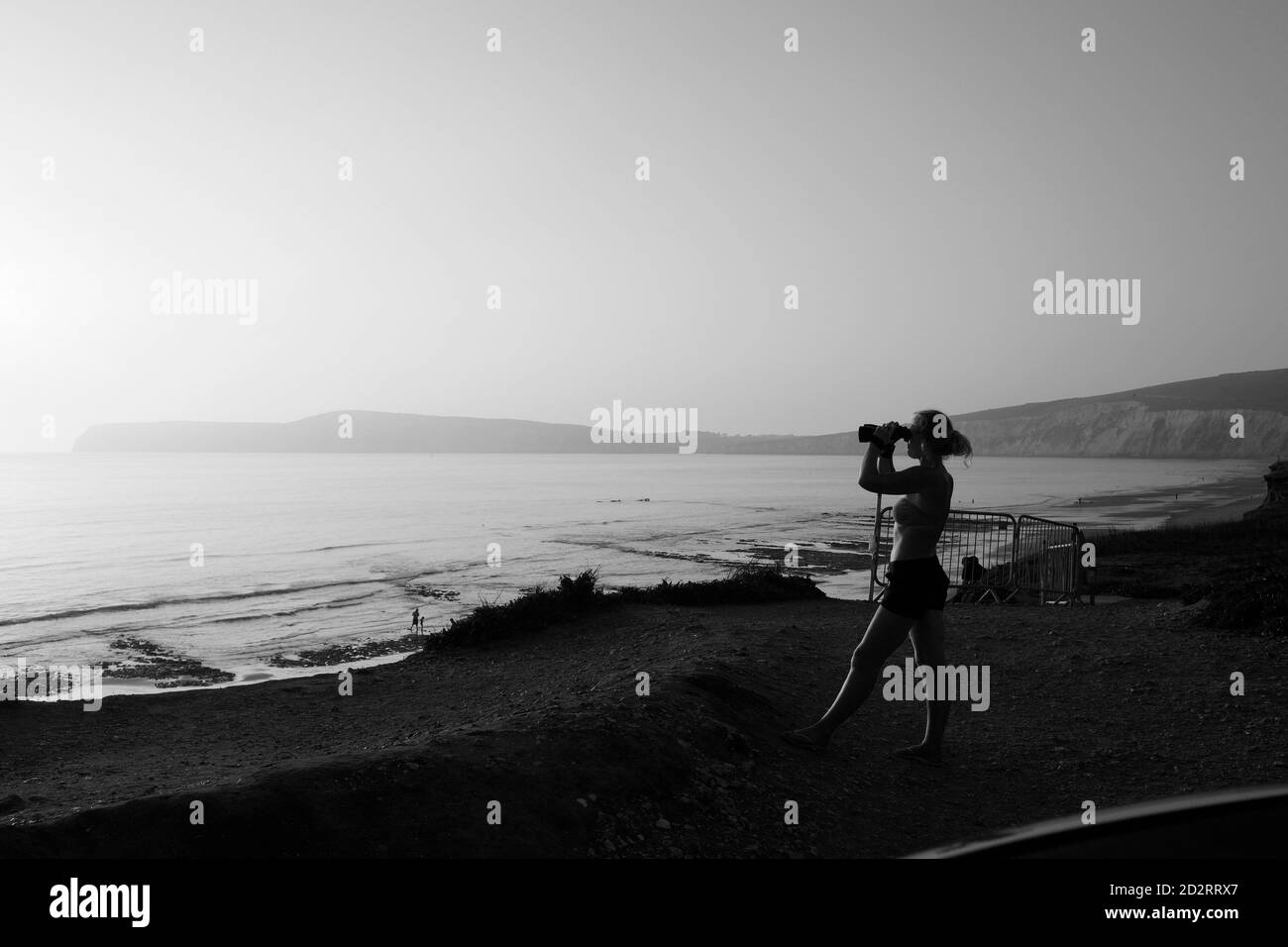 Femme avec des jumelles donnant sur la mer pendant le coucher du soleil à Compton Bay, île de Wight Banque D'Images