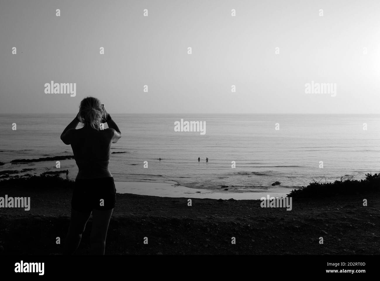 Femme avec des jumelles donnant sur la mer pendant le coucher du soleil à Compton Bay, île de Wight Banque D'Images