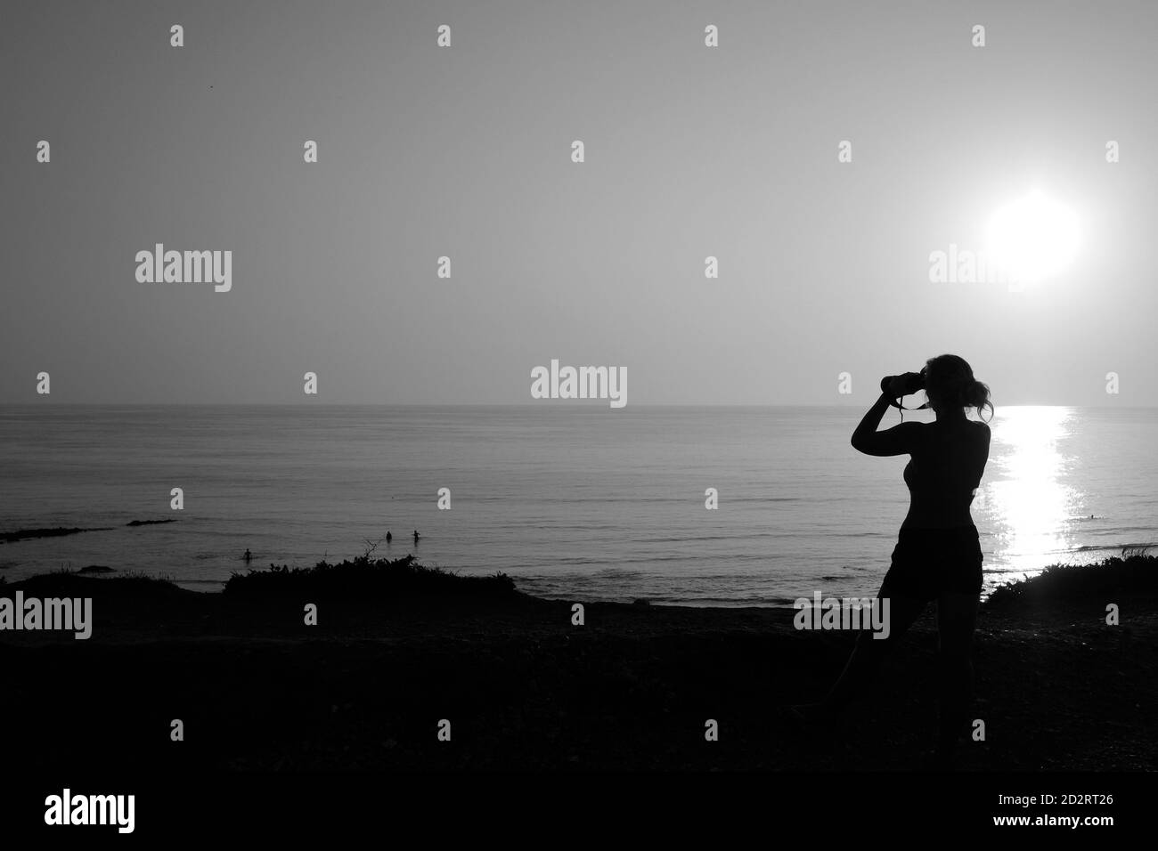 Femme avec des jumelles donnant sur la mer pendant le coucher du soleil à Compton Bay, île de Wight Banque D'Images
