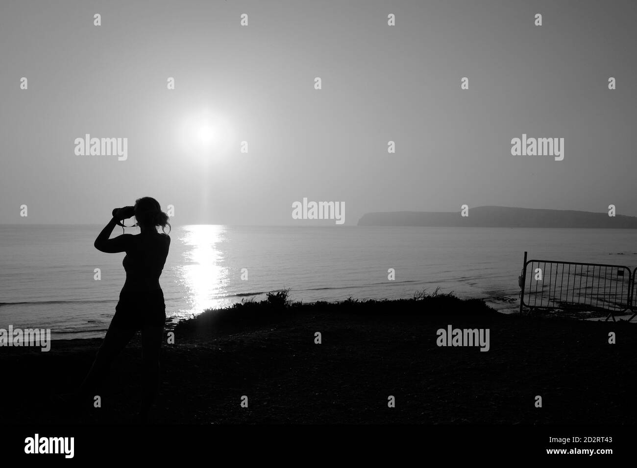 Femme avec des jumelles donnant sur la mer pendant le coucher du soleil à Compton Bay, île de Wight Banque D'Images