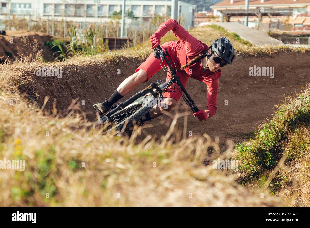 Sportswoman en casque noir et vêtements de sport rouges avec lunettes de vélo de montagne sur la piste d'entraînement Banque D'Images