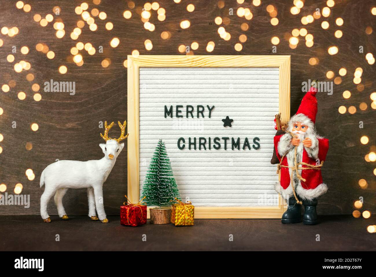 Nouvelle année composition de cerf blanc, Père Noël, lumières, arbre, boîte-cadeau, tableau de feutre avec texte Joyeux Noël sur fond de bois foncé carte de vacances Banque D'Images