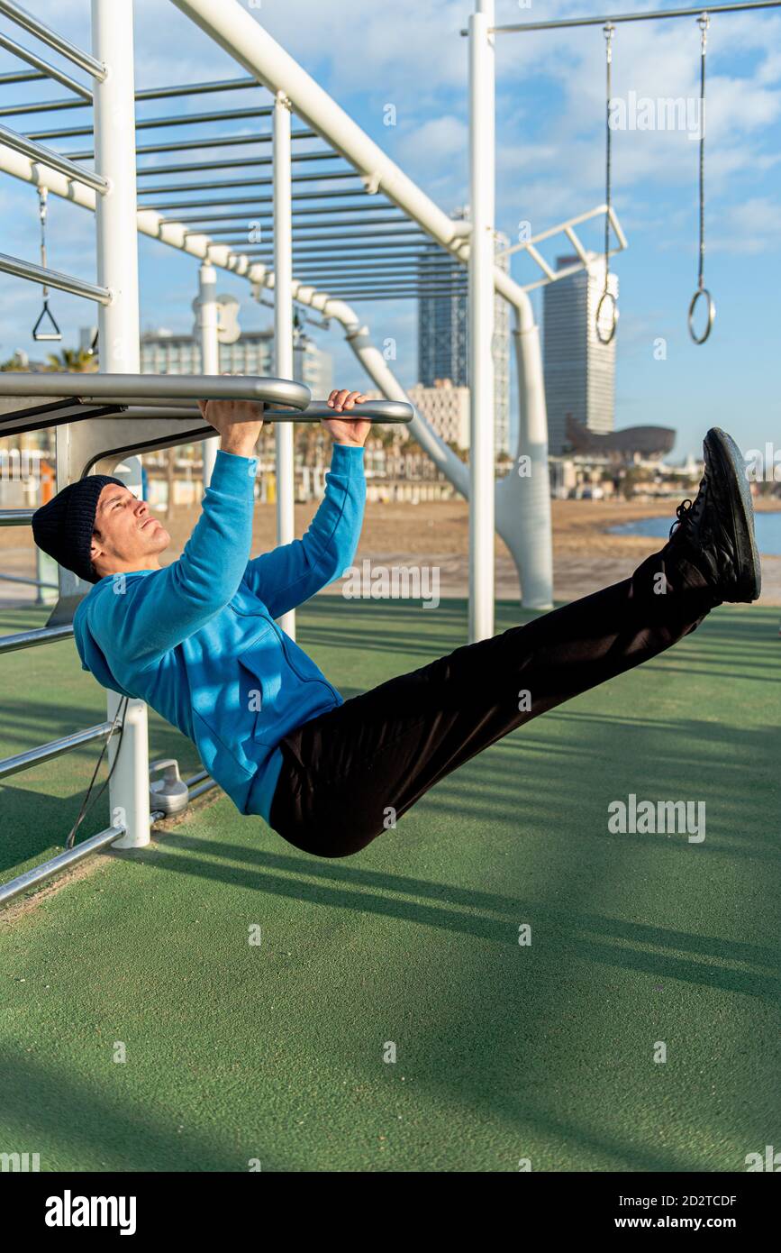 Vue latérale d'un homme sportif concentré en vêtements d'activité suspendus  exercice d'élévation de jambe sur les barres métalliques pendant  l'entraînement de fitness sur terrain de sport Photo Stock - Alamy
