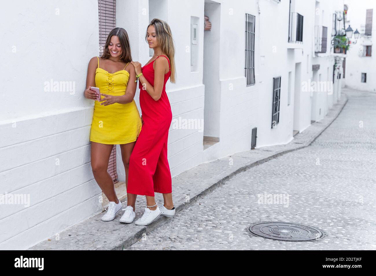 Des amies positives portent des vêtements d'été debout près du bâtiment rue étroite et lecture de messages sur téléphone portable pendant l'été promenez-vous Banque D'Images