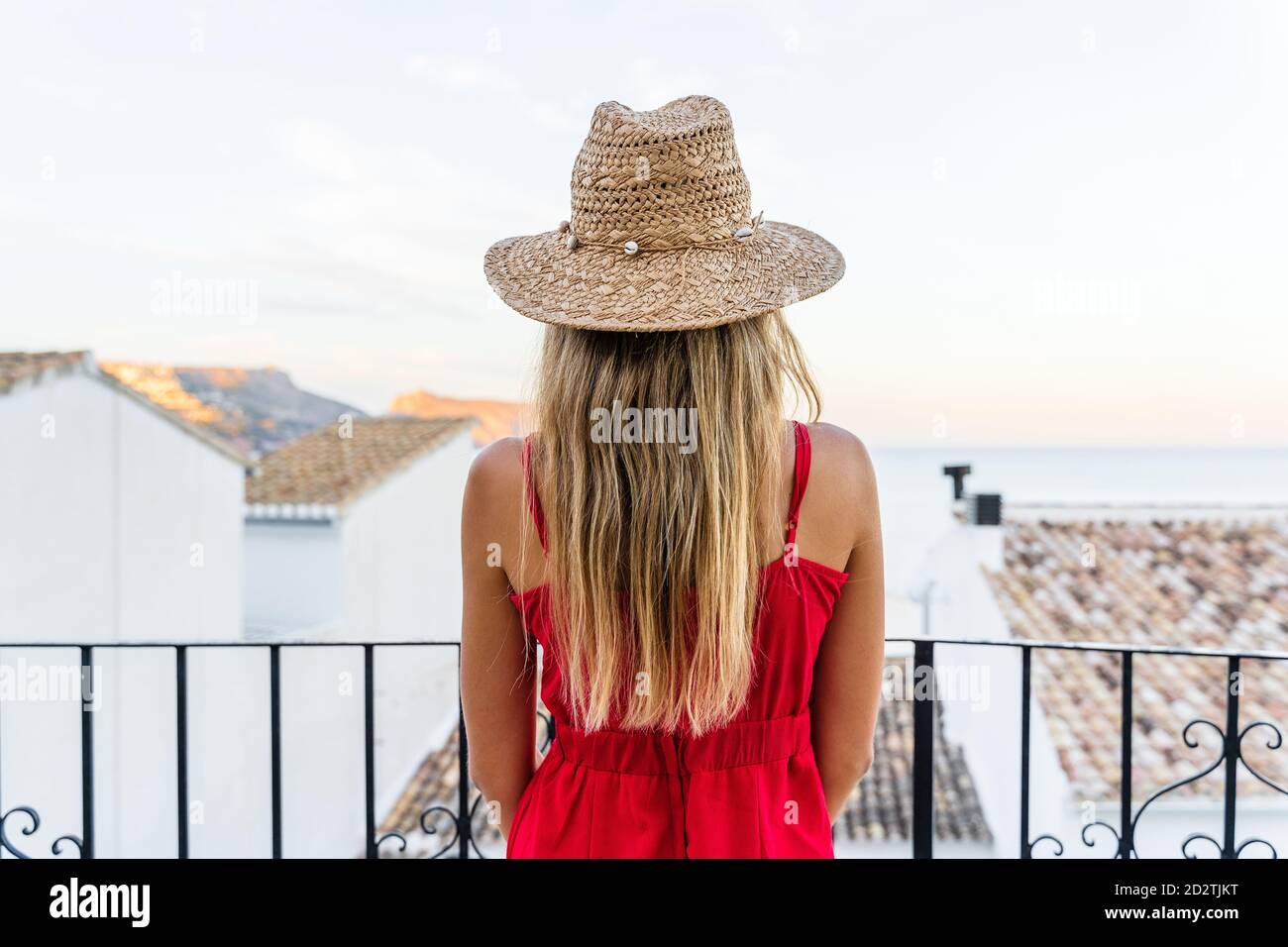 Vue arrière d'une touriste féminine méconnue debout avec chapeau de paille  dans la main levée sur la terrasse et profiter des vacances d'été pendant  admirez le paysage urbain incroyable Photo Stock -