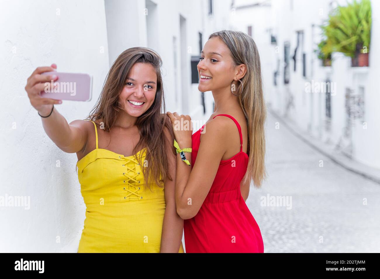 Des amies positives portent des vêtements d'été debout près du bâtiment rue étroite et lecture de messages sur téléphone portable pendant l'été promenez-vous Banque D'Images