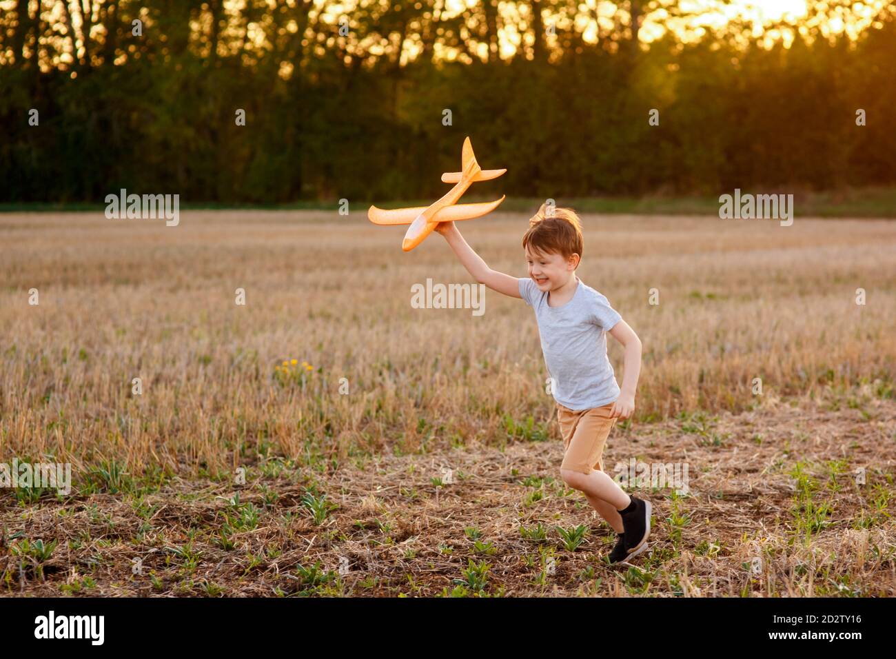 Un enfant heureux court avec un avion jouet sur un fond de coucher de soleil sur un champ. Le concept d'une famille heureuse. Rêves d'enfance Banque D'Images