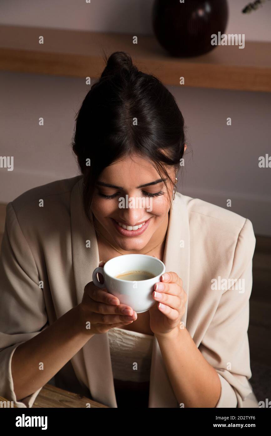De dessus de positive jeune femme rêveuse avec une tasse de café aromatique assis à la table et donnant sur l'extérieur tout en se relaxant à la maison Banque D'Images