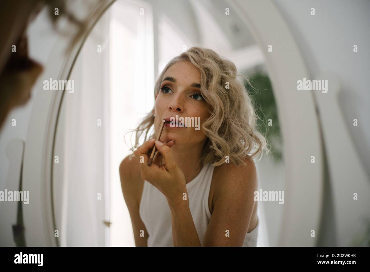 Angle bas de charmante femme appliquant le crayon à lèvres et de faire maquillage à la maison tout en réfléchissant dans le miroir Banque D'Images