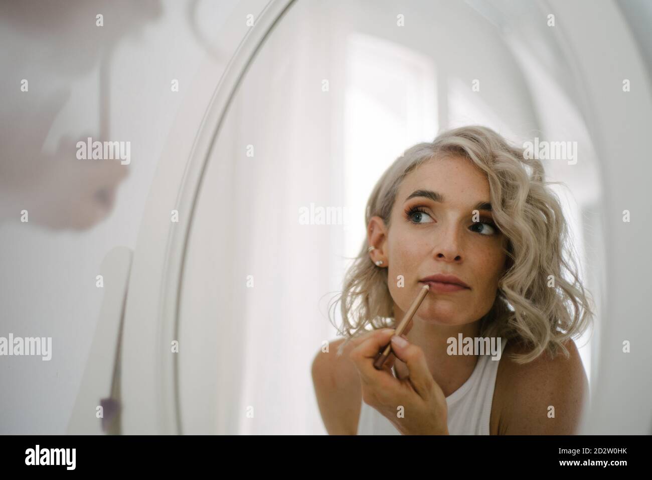 Angle bas de charmante femme appliquant le crayon à lèvres et de faire maquillage à la maison tout en réfléchissant dans le miroir Banque D'Images