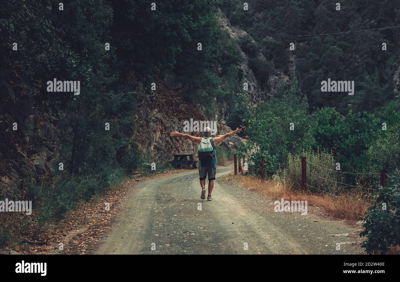 Homme âgé au milieu de la route dans la forêt. Image d'un randonneur de l'arrière dans la nature avec les mains ouvertes. Banque D'Images Homme âgé au milieu de la route dans la forêt. Image d'un randonneur de l'arrière dans la nature avec les mains ouvertes. Banque D'Images