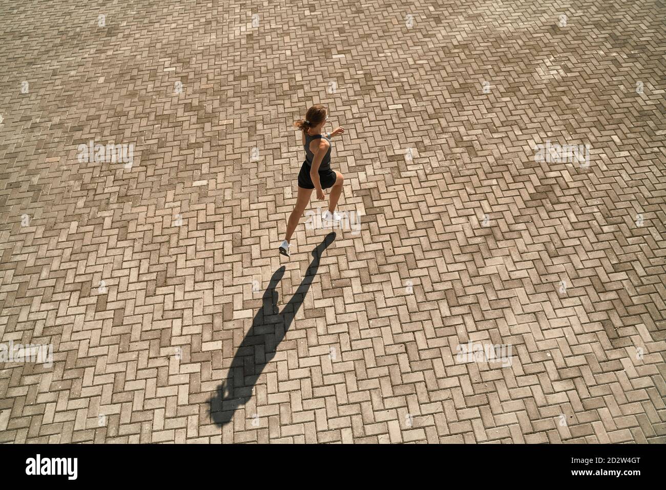 Du haut du corps de la femme active et mince dans les vêtements de sport course rapide sur la place pavée par beau temps Banque D'Images