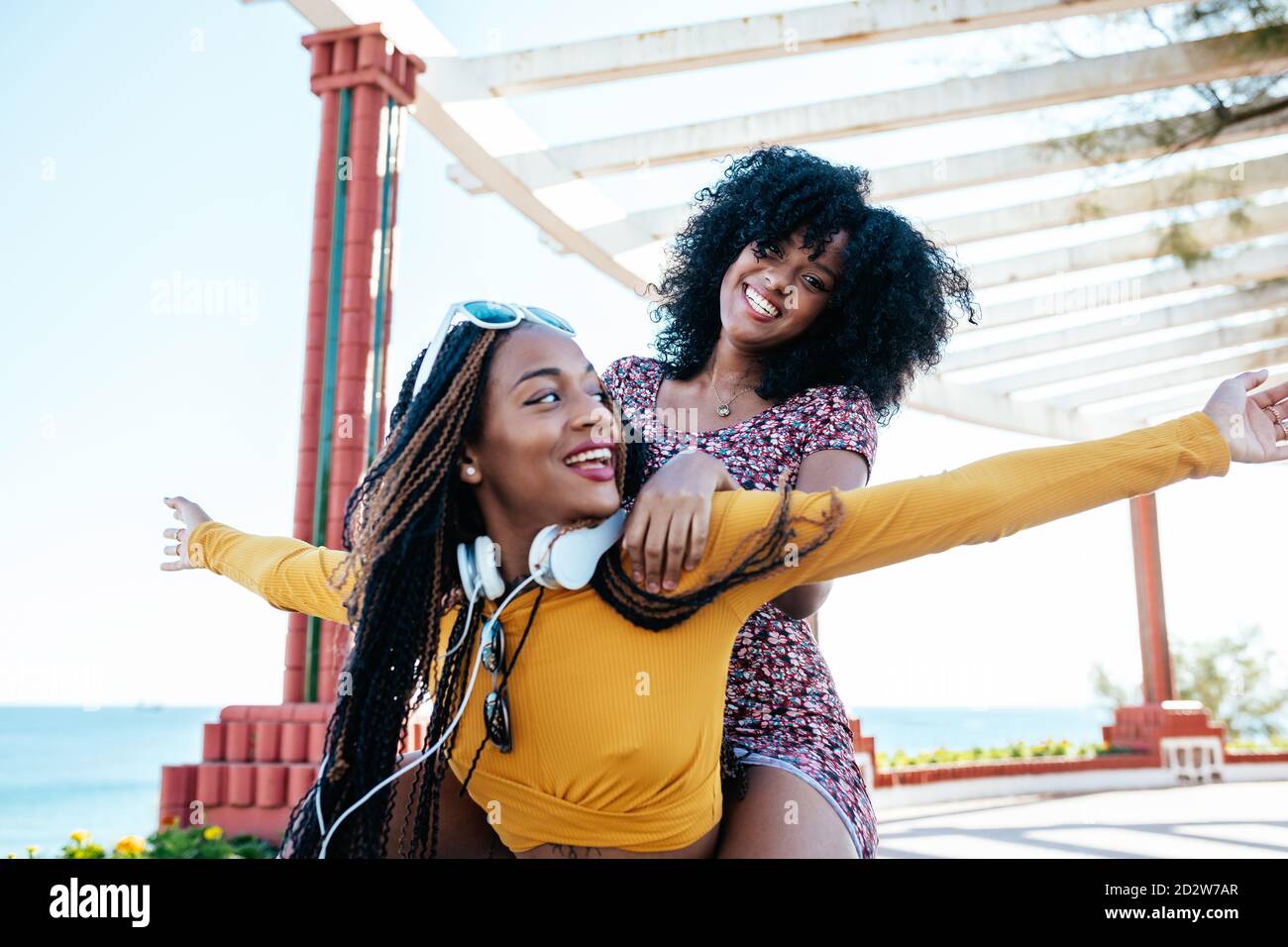 Une femme ethnique gaie aux cheveux bouclés a ravie une amie avec des tresses tout en s'amusant sur la promenade le week-end en été Banque D'Images