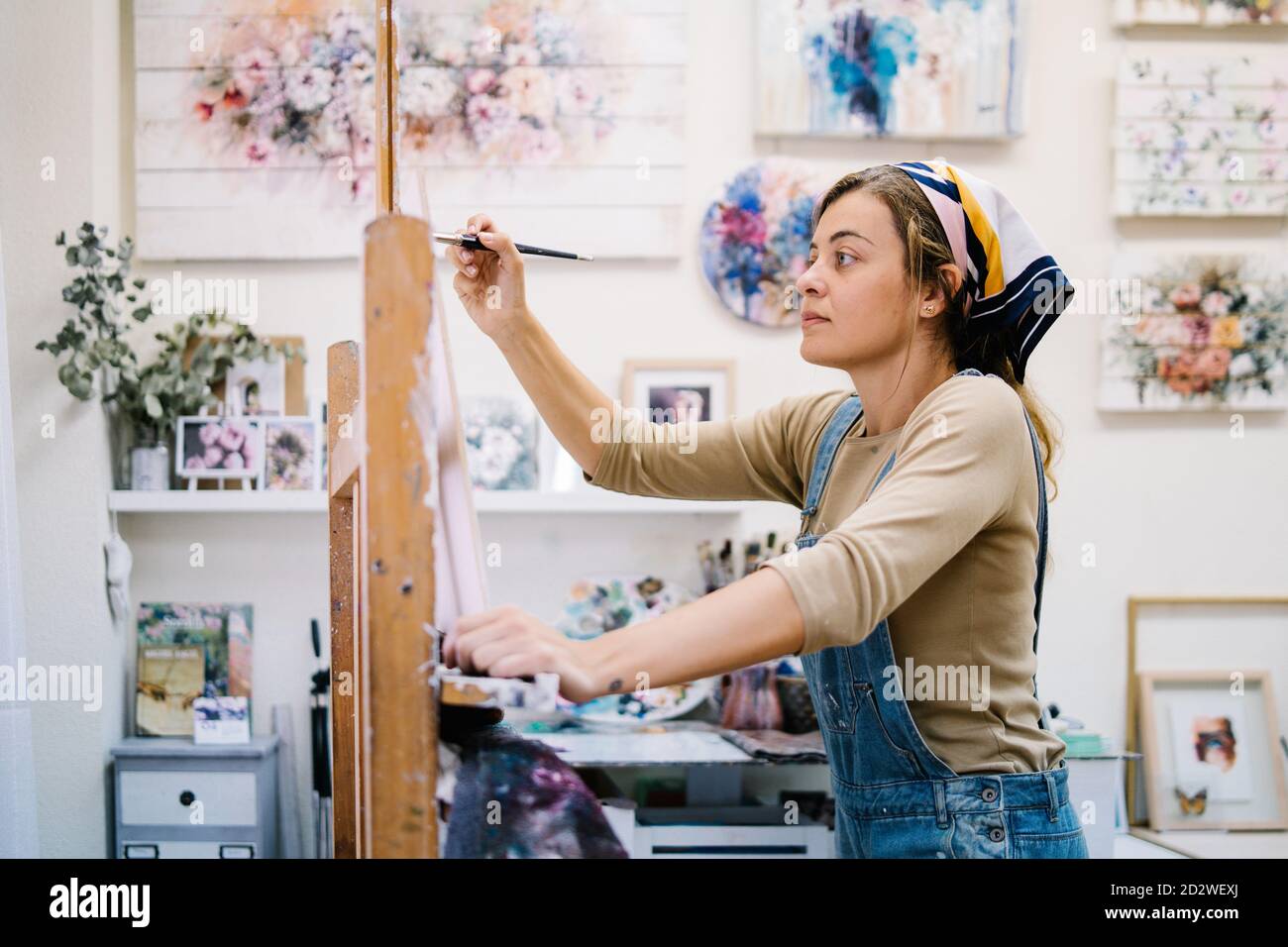 Vue latérale d'une artiste féminine se tenant près du chevalet et du dessin une image colorée avec des peintures tout en travaillant dans un atelier créatif Banque D'Images
