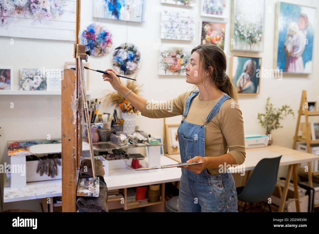 Vue latérale d'une artiste féminine se tenant près du chevalet et du dessin une image colorée avec des peintures tout en travaillant dans un atelier créatif Banque D'Images