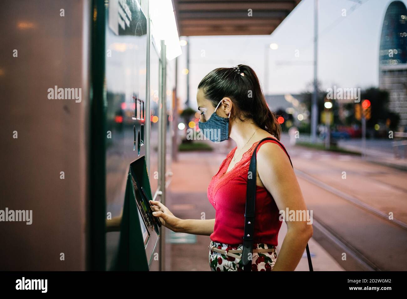 Vue latérale d'une jeune femme à l'achat d'un masque de protection billet pour les transports en commun sur le distributeur automatique Banque D'Images