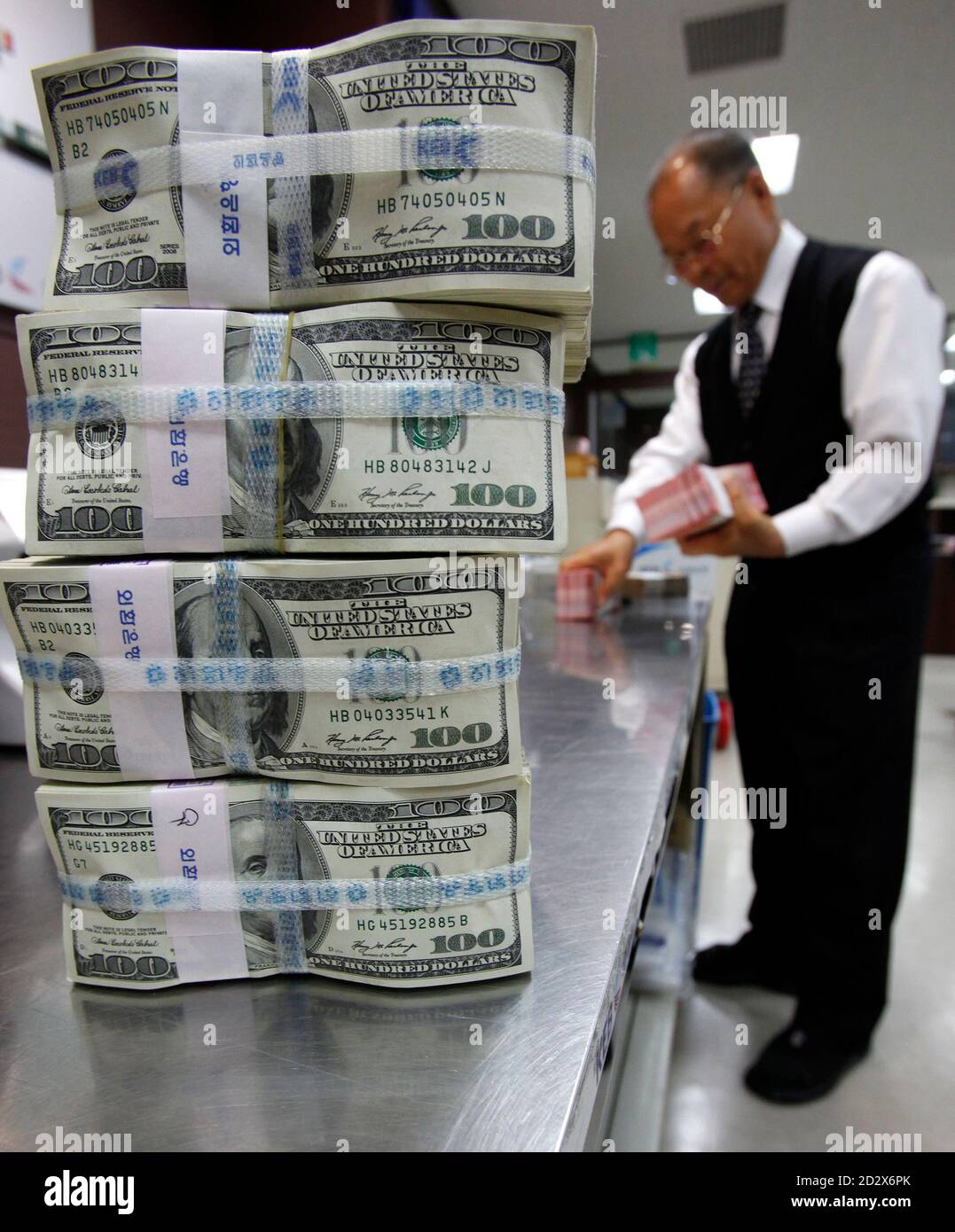 Un employé de la Korea Exchange Bank compte les devises étrangères à côté de piles de billets de cent dollars au siège de la banque à Séoul le 3 novembre 2009. Les réserves de change de la Corée du Sud ont augmenté de près de 10 milliards de dollars en octobre, pour atteindre le deuxième plus grand montant jamais enregistré alors que la quatrième économie asiatique s'est rapidement retirée de la crise financière mondiale. REUTERS/JO Yong-Hak (CORÉE DU SUD) Banque D'Images
